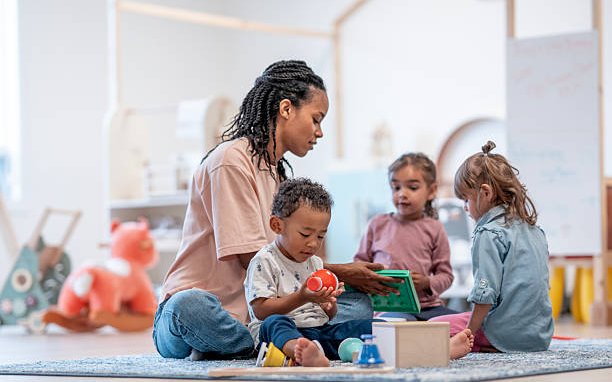 A teacher sitting on the floor playing with three preschoolers and a set of shape toys